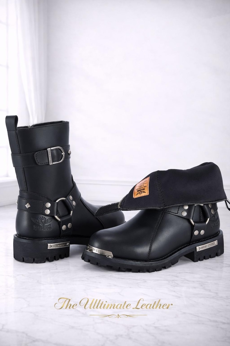 May include: Black leather motorcycle boots with silver-tone hardware, including buckles, rings, and studs. One boot is upright, the other has a folded-down cuff. The boots have a thick sole and a small metal plate with text. The Ultimate Leather is written at the bottom.