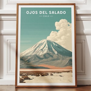 May include: A framed art print featuring a mountain landscape with the text "OJOS DEL SALADO - CHILE". The artwork depicts a snow-capped mountain under a blue sky with fluffy clouds. The frame is a warm brown color.