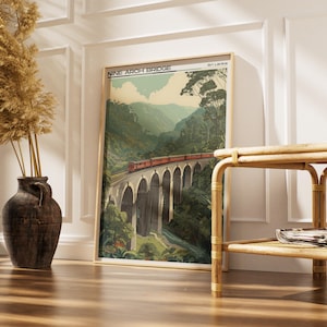 May include: A framed print of the Nine Arch Bridge in Sri Lanka. The artwork shows a red train crossing the bridge, set against green mountains and a blue sky. The print is in a wooden frame.