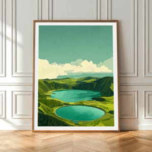 May include: A framed art print depicting a landscape with two turquoise lakes set in green hills, under a light blue sky with white clouds. The artwork is displayed in a room with white walls and a wooden floor.