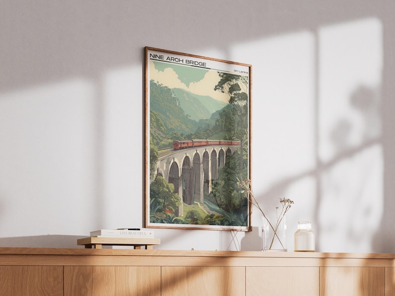 May include: A framed print of the Nine Arch Bridge in Sri Lanka. The image shows a red train on the bridge, surrounded by green hills and trees. The print has a vintage style, reminiscent of travel posters.