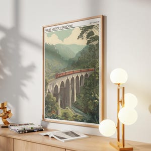 May include: Framed art print of the Nine Arch Bridge in Sri Lanka. The image shows a red train crossing the bridge, set against green mountains and trees. The print is in a wooden frame, with the text "Nine Arch Bridge" at the top.