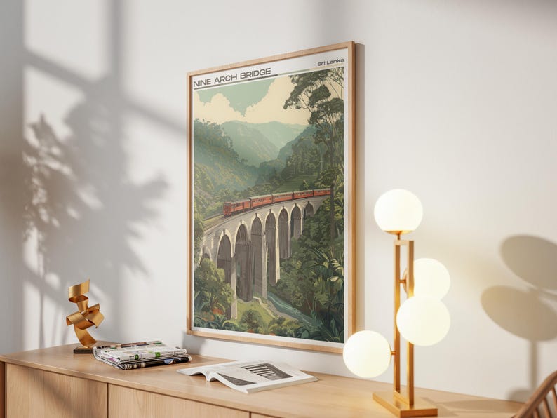 May include: Framed art print of the Nine Arch Bridge in Sri Lanka. The image shows a red train crossing the bridge, set against green mountains and trees. The print is in a wooden frame, with the text "Nine Arch Bridge" at the top.