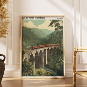 May include: A framed print of the Nine Arch Bridge in Sri Lanka. The artwork shows a red train crossing the bridge, set against a backdrop of green mountains and foliage. The print has a vintage aesthetic.