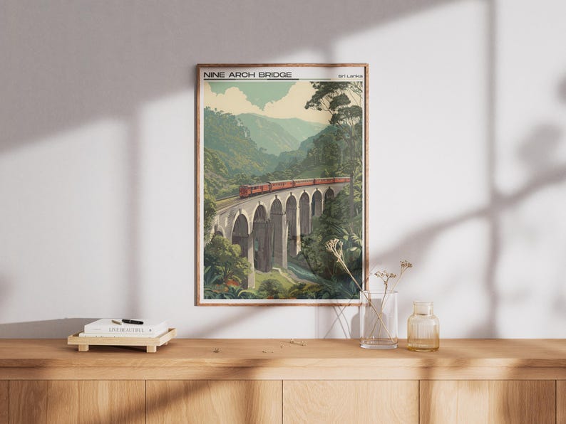 May include: A framed print of the Nine Arch Bridge in Sri Lanka. The artwork shows a red train crossing the bridge, surrounded by green foliage and mountains. The print is displayed on a wooden surface.