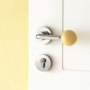 May include: A modern door handle set with a polished chrome finish. The handle features a cylindrical, light yellow knob. The set includes a matching round door lock and keyhole, mounted on a white door.