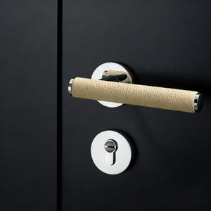 May include: A modern door handle set with a textured, light tan grip and polished chrome accents. The handle is cylindrical and mounted on a circular chrome backplate. A matching keyhole escutcheon is below.