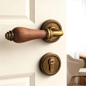 May include: A vintage-style door handle set with a wooden handle and antique brass finish. The set includes a lever handle and a keyhole escutcheon, both featuring intricate detailing. The door handle is mounted on a white door.