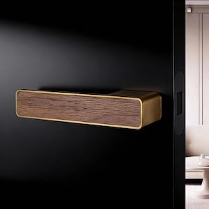May include: A rectangular door handle with a wood grain center and gold-colored trim. The handle is mounted on a black door. The wood grain is a medium brown color. The gold trim is a thin border around the wood grain.
