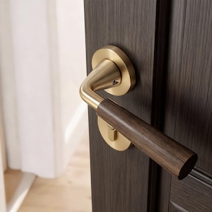 May include: A brass door handle with a dark wood grip, mounted on a dark brown wooden door. The handle's design is modern and sleek. The door is slightly open, showing a white curtain in the background.