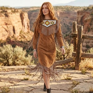 May include: A brown suede dress with long sleeves and fringe detailing. The dress features a geometric pattern on the neckline and fringe along the sleeves and hem. The dress is knee-length and is paired with black boots.