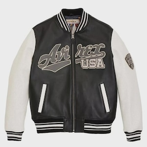 May include: Black leather bomber jacket with white perforated sleeves. The jacket features the text "Air Rex USA" on the chest and a patch on the right sleeve. The collar, cuffs, and hem have black and white striped detailing.