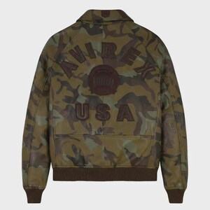 May include: A camouflage-patterned leather jacket with the word "AVIREX" arched across the back, along with a circular emblem and the word "USA" below. The jacket features a brown collar, cuffs, and hem.