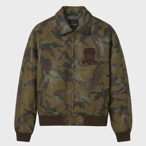 May include: A camouflage-patterned leather jacket in shades of green, brown, and tan. The jacket features a collared neckline, a zipper closure, and a brown ribbed hem and cuffs. A brown patch is on the chest. The brand name "AVIREX" is visible on the collar.