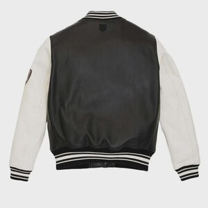 May include: Black leather varsity jacket with white perforated sleeves. The jacket features a black and white striped collar, cuffs, and hem. A small emblem is visible on the chest. The back of the jacket is solid black leather.