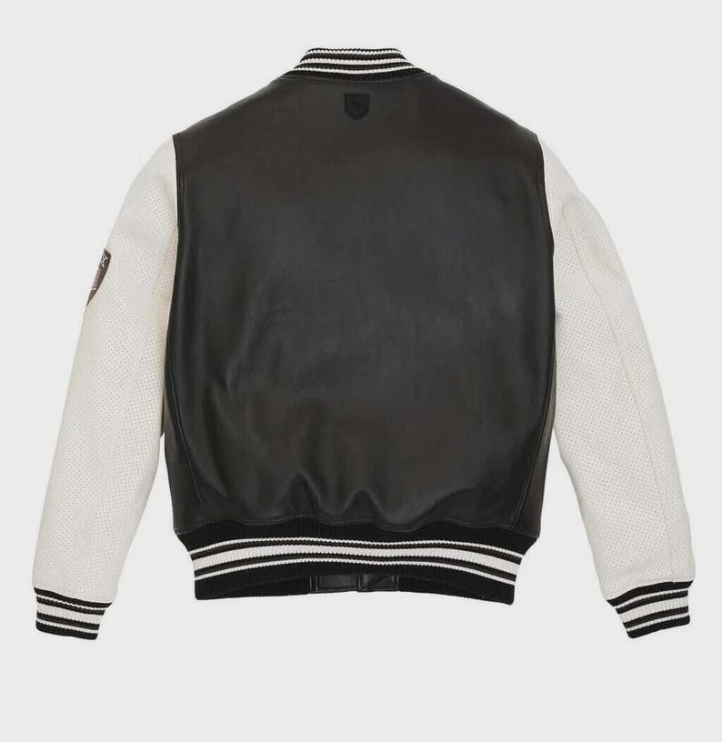 May include: Black leather varsity jacket with white perforated sleeves. The jacket features a black and white striped collar, cuffs, and hem. A small emblem is visible on the chest. The back of the jacket is solid black leather.