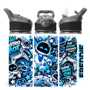 May include: A white water bottle with a grey lid and straw, featuring a blue and black graphic print of Astro Bot characters, game controllers, planets, and stars. The text reads Astro Bot, Play Explore Discover, Game Mode On, and Freddie.