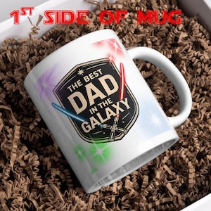 May include: A white ceramic mug featuring a black shield-shaped emblem with the text THE BEST DAD IN THE GALAXY. The design includes two crossed lightsabers in red and blue, surrounded by colourful starburst accents on a white background.