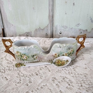 May include: A vintage porcelain sugar bowl with two compartments and a matching spoon. The bowl features hand-painted yellow roses and gold accents on the handles. The background is a light green and white.