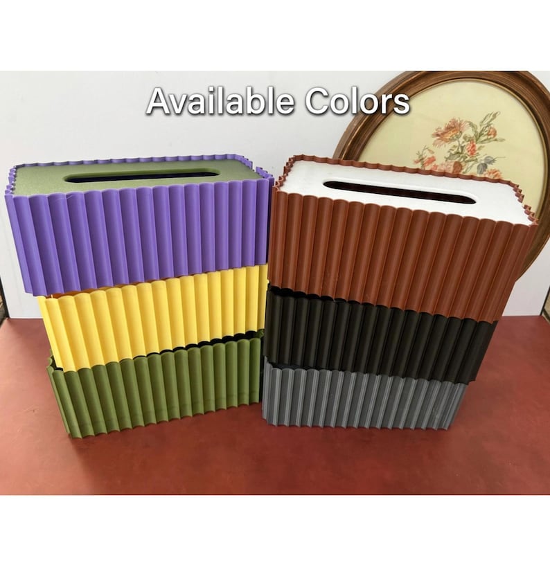 May include: Two stacks of rectangular tissue box covers with a vertical ribbed texture. The left stack features purple, yellow, and olive green covers. The right stack features brown, black, and gray covers. The text Available Colors is visible.