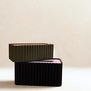 May include: Two rectangular tissue box holders, one stacked on top of the other. The top box is olive green, and the bottom box is black. Both have a ribbed design. The interior of the top box is pink.
