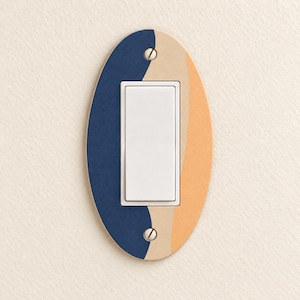 May include: An oval light switch plate featuring a color-blocked design with a dark blue section on the left, a thin beige stripe in the center, and a light orange section on the right. The plate includes a white rocker switch and two screws.