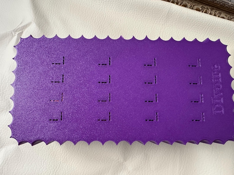 May include: A rectangular purple foam display board with a scalloped edge, featuring four columns of four vertical slits for organizing items. The word "Difoire" is embossed on the right side of the textured surface of this storage accessory.