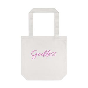 May include: A white tote bag with a rectangular body and a handle. The word "Goddess" is written in a cursive, pink font on the front of the bag. The bag is made of a sturdy fabric.