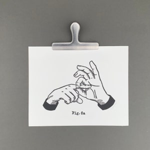 May include: A black and white illustration of two hands in a gesture, held by a silver metal clip. The illustration is on a white paper with the text "Fig. 6a". The clip is attached to a gray background.