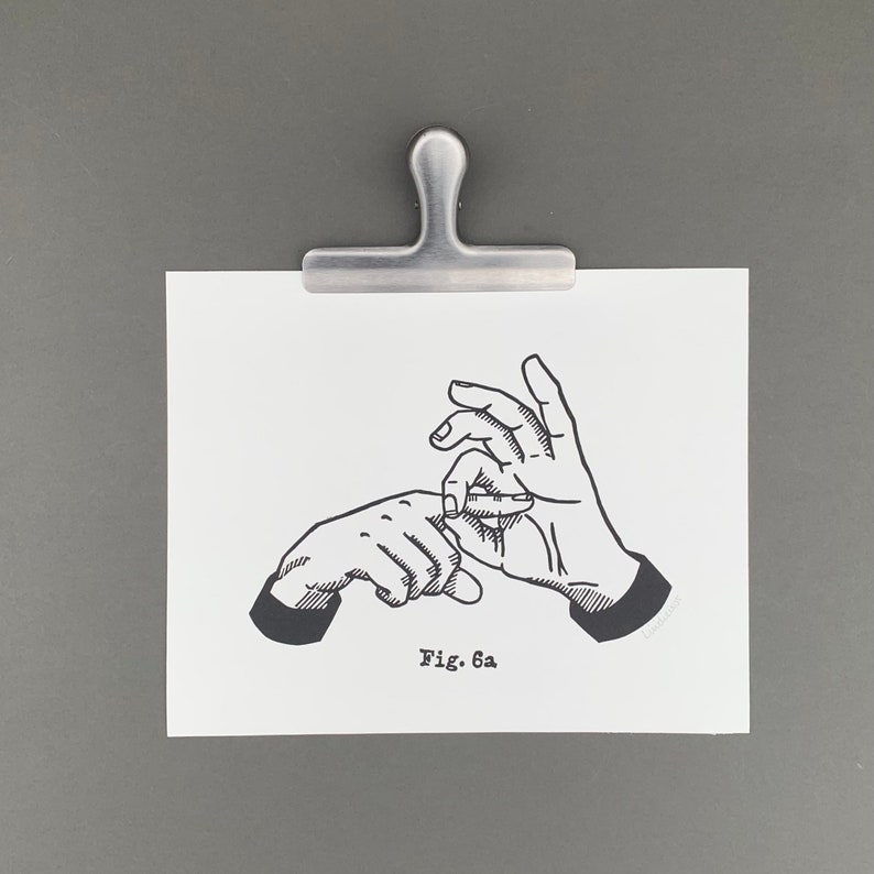 May include: A black and white illustration of two hands in a gesture, held by a silver metal clip. The illustration is on a white paper with the text "Fig. 6a". The clip is attached to a gray background.