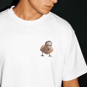 May include: White t-shirt featuring a humorous graphic of a person's face on a chicken body. The shirt has short sleeves and a crew neck. The graphic is in the center of the shirt.