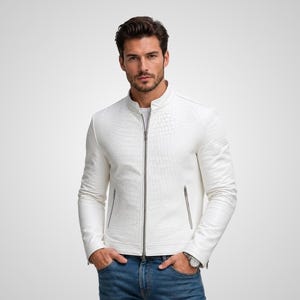 Può includere: Una giacca in pelle bianca con motivo testurizzato in pelle di coccodrillo, dotata di colletto alla coreana, chiusura frontale con zip in metallo argentato e due tasche laterali con zip, abbinata a jeans blu e un orologio da polso argentato.