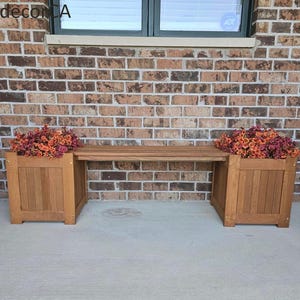 May include: A wooden bench featuring two integrated square planters on each end, each filled with vibrant orange and purple flowers. The bench has a slatted seat design and a natural wood finish, positioned against a brown brick wall.