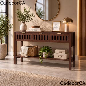 May include: A dark brown wooden console table with three drawers featuring vertical slat detailing and gold-toned hardware. The table has a lower shelf holding a woven basket with a white cloth, a potted green plant, and two stacked beige boxes.