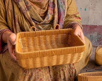 Peut inclure: Un panier rectangulaire en osier tressé de couleur brun clair, doté d'un bord structuré et de deux petites boucles intégrées sur le dessus pour la suspension. Le panier présente un motif de tressage serré et uniforme sur les côtés et la base.