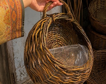 Peut inclure: Un panier rond à suspendre au mur, fabriqué en branches d'osier tressées de couleur brun foncé. Le panier présente un dos plat, une façade incurvée et une poignée supérieure solide. Une doublure en plastique transparent tapisse l'intérieur.