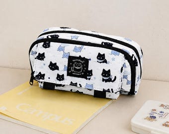 Peut inclure: Trousse blanche avec fermeture éclair noire et illustrations de chats noirs. La trousse a un écusson de chat noir et blanc et est posée sur un cahier jaune. La trousse mesure environ 20 cm de long.