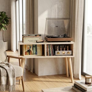 May include: A rectangular travertine console table with four light wood legs. The top holds a walnut-finished record player with a clear dust cover. The two open shelves contain vinyl records, including one labeled The Silent Forest, and an amplifier.