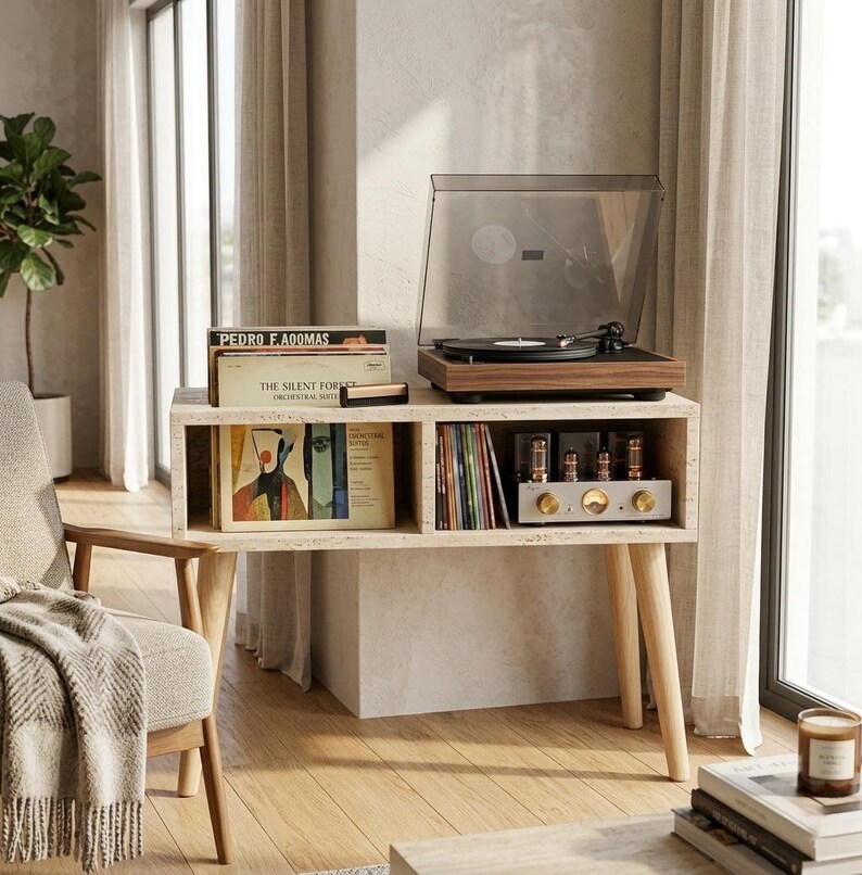 May include: A rectangular travertine console table with four light wood legs. The top holds a walnut-finished record player with a clear dust cover. The two open shelves contain vinyl records, including one labeled The Silent Forest, and an amplifier.