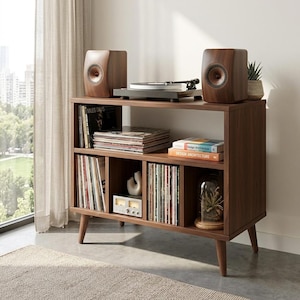 May include: A dark wood media unit with a record player, speakers, and vinyl records. The unit has a mid-century modern design with angled legs. Two speakers are on top, and the unit is filled with records and books. The unit is approximately 100cm wide.
