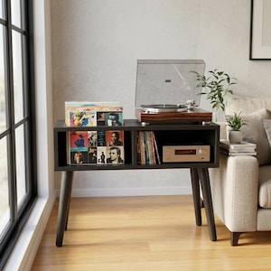 May include: A dark brown wooden media console with four tapered legs, featuring an open top compartment for vinyl records, a side shelf for additional records, and a flat surface holding a wood-grain turntable with a clear plastic lid.