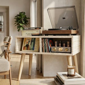 May include: A beige travertine console table with four light wood tapered legs, featuring two open storage compartments. The top holds a wooden turntable with a clear lid. The shelves contain vinyl records and a silver vacuum tube amplifier.