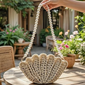 May include: A beige, seashell-shaped handbag with a pearl beaded handle. The bag is made of woven material and has a scalloped edge. The handle is a strand of white pearls. The bag is sitting on a wooden table.