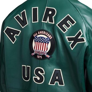 May include: Green leather jacket with white and black lettering spelling out "AVIREX" and "USA". A circular patch features the American flag and the words "ALL AMERICANS" and "ESTABLISHED 1975".