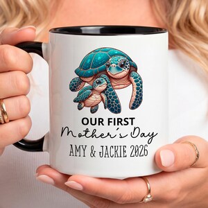 Puede incluir: Una taza de cerámica blanca con asa negra y el texto "But First, Coffee" en negrita negra. La taza se encuentra sobre un fondo borroso, sugiriendo un ambiente acogedor.