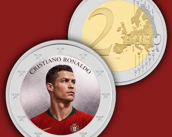 May include: A commemorative two-euro coin featuring a portrait of Cristiano Ronaldo in a red jersey on the front, with the text Cristiano Ronaldo arched above. The reverse side shows the standard two-euro map design with the number two and Euro text.