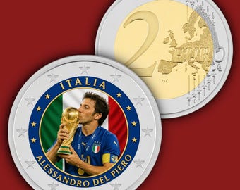 May include: A commemorative two-euro coin featuring a colourised portrait of Alessandro Del Piero kissing the FIFA World Cup trophy against the Italian flag. The coin is surrounded by twelve stars and the text ITALIA ALESSANDRO DEL PIERO.