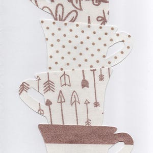 May include: Stack of four white teacups with brown patterns. The top cup has a floral design, the second has polka dots, the third has arrows, and the bottom has brown stripes.