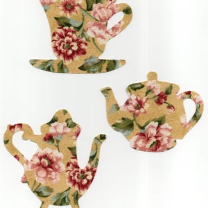 May include: Three die-cut shapes: a teacup and saucer, and two teapots. Each is covered in a floral pattern with red, pink, and green flowers on a tan background. The teacups and teapots are likely for crafting or scrapbooking.