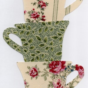 May include: Three fabric teacup cutouts. The top cup has a cream background with red floral and green stripe patterns. The middle cup is green with a leaf pattern. The bottom cup has a cream background with red and blue floral patterns.